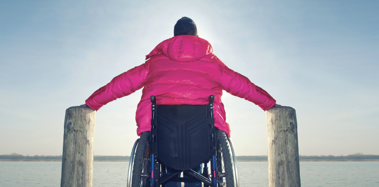MAn in a wheelchair sitting in front of a beautiful lake.