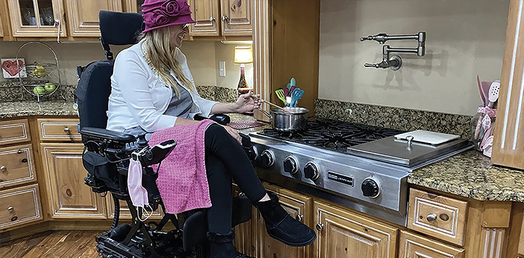 A woman who uses a raised wheelchair is cooking on her stove.